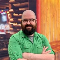 An image of the author with a log cabin background.