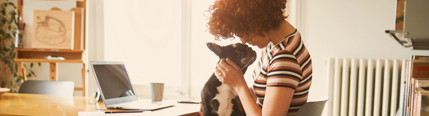 A woman sitting at a desk with a small dog on her lap